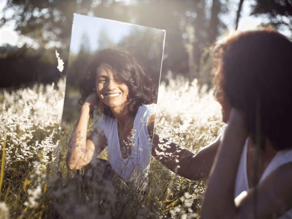 Uśmiechnięta kobieta z równymi zębami patrząca na swoje odbicie w lustrze